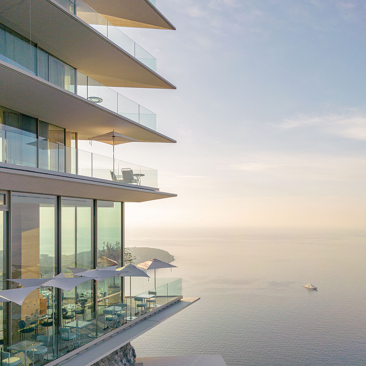 A view of The Maybourne Riviera from the side, with the Riviera Restaurant at the bottom floor, ant the infinite sea in the background.