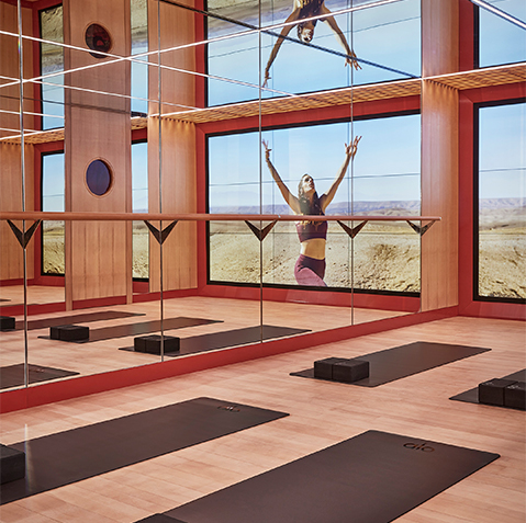The virtual studio features wood panelled floors and floor to ceiling mirrors. Black ALO Yoga mats line the floor