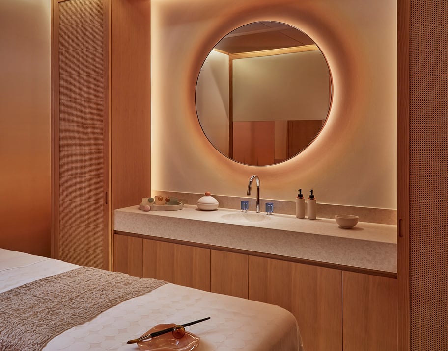 Glowing spa treatment room mirror facing a massage bed, the room features wooden wall panelling and a marble sink