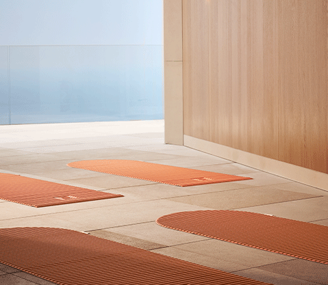 Terrace with orange yoga mats neatly laid out on pale stone tiles, bordered by a wood-panelled wall and glass balustrade overlooking the sea.
