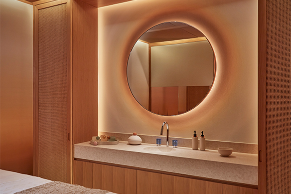 Glowing spa treatment room mirror facing a massage bed, the room features wooden wall panelling and a marble sink